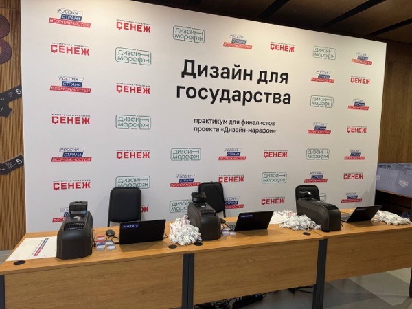 Три рабочих места печати бейджей с принтерами, ноутбуками и лентами перед пресс-волом мероприятия