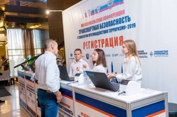 Сотрудница передаёт именной бейдж гостю на стойке регистрации транспортного форума в холле отеля