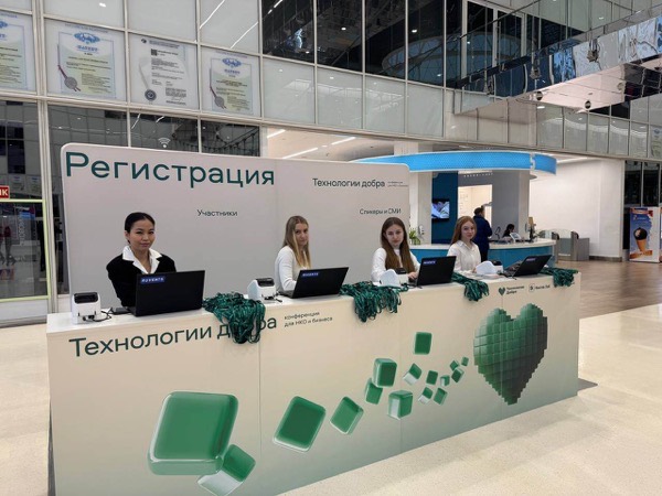Четыре сотрудницы на стойке регистрации форума «Технологии добра» с зелёными лентами для бейджей