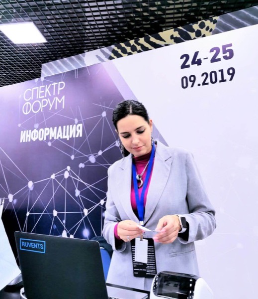 Сотрудница информационной стойки форума «Спектр» проверяет бейдж рядом с ноутбуком