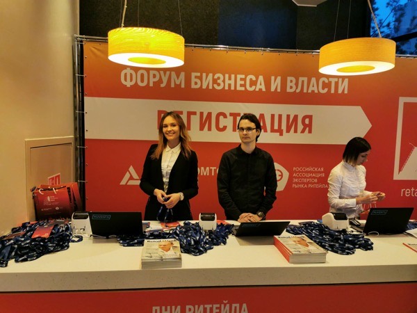Трое сотрудников за стойкой «Форума бизнеса и власти» с синими лентами для бейджей и ноутбуками