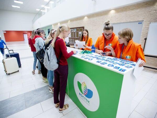 Две сотрудницы в фирменных жилетах регистрируют участниц форума «Восток» за стойкой аккредитации