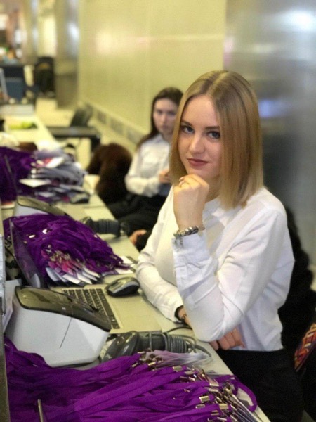 Сотрудница позирует у стойки со стопками фиолетовых лент для бейджей