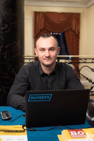 Портрет сотрудника за столом с ноутбуком Ruvents на фоне портьер и лестничных перил