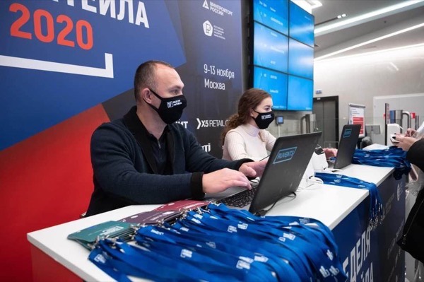 Сотрудники в масках работают за ноутбуками на стойке регистрации форума «Неделя ритейла 2020»