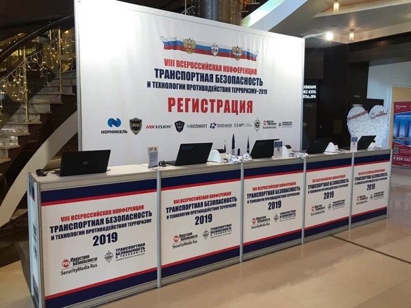 Пустая стойка регистрации с пятью ноутбуками под баннером конференции по транспортной безопасности
