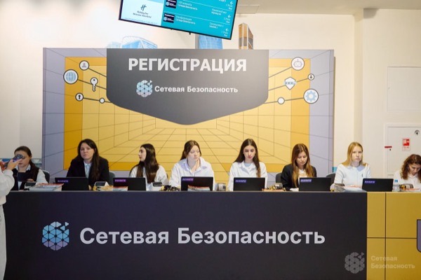Ряд рабочих мест с ноутбуками и принтерами за брендированной стойкой регистрации конференции