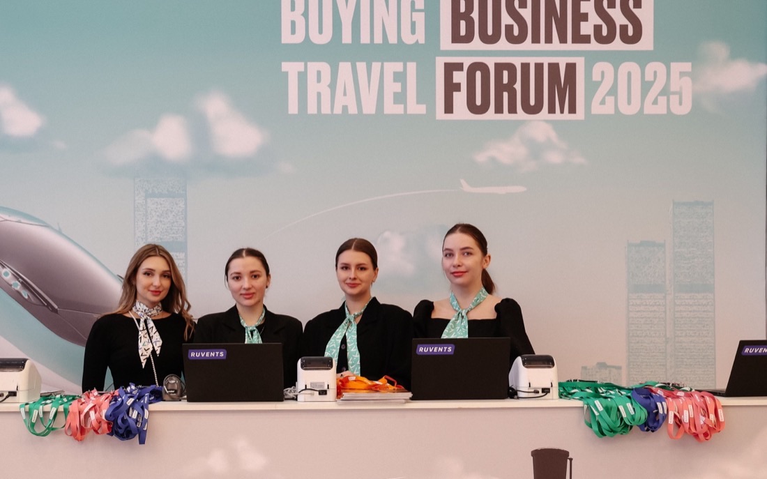 Четыре сотрудницы регистрации за стойкой Buying Business Travel Forum 2025 с лентами для бейджей и принтерами