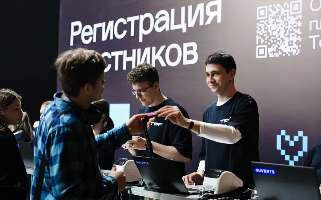 Молодые сотрудники регистрации выдают бейджи участникам у экрана с надписью «Регистрация участников» и QR-кодом